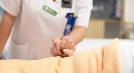 En vårdgivare håller en patient i handen.